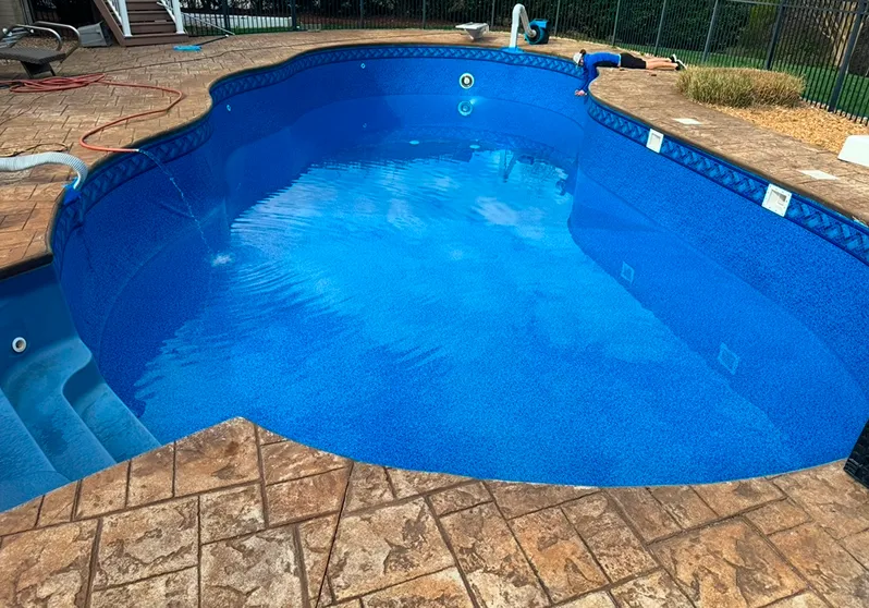 A swimming pool featuring a blue liner and a smooth concrete floor, reflecting sunlight.