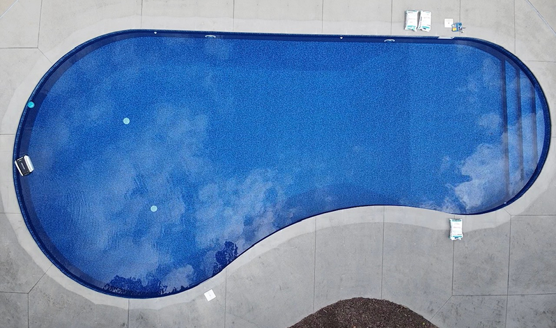Overhead view of a swimming pool surrounded by clear blue water under a bright blue sky.