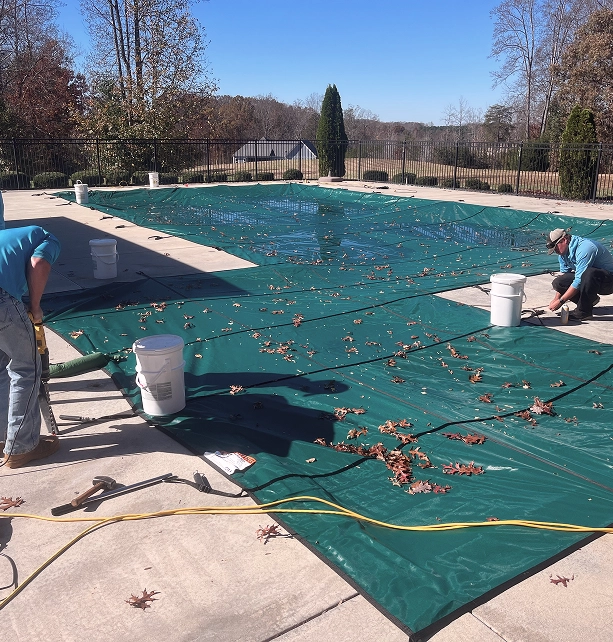 Two men are collaborating to install a pool cover in a residential backyard setting.