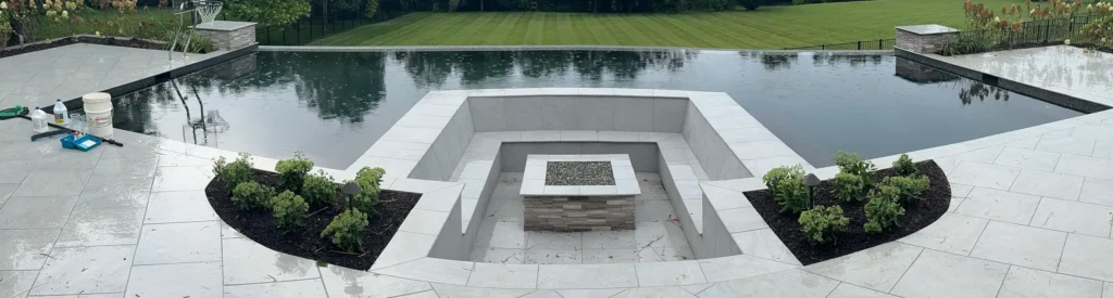 Modern infinity-edge pool with built-in sunken fire pit lounge and tiled patio