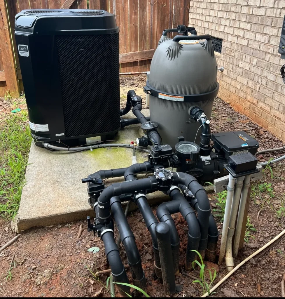 Pool equipment system with black pipes, pump, and filtration unit beside a brick wall