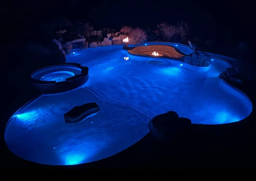 Luxury backyard pool illuminated with blue LED lights at night with fire features