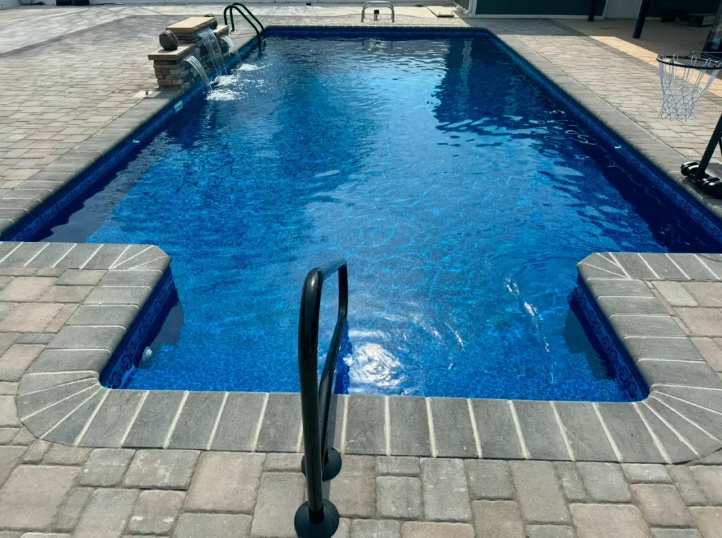 Rectangular swimming pool with water feature and stone paver deck