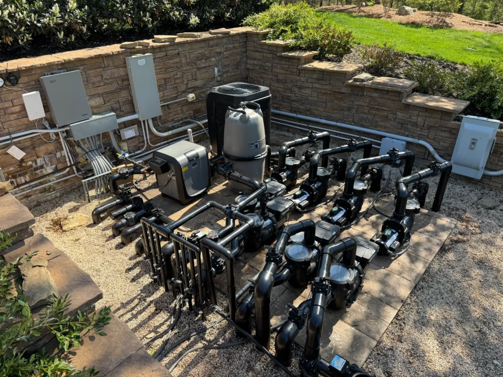 Advanced pool equipment system with multiple pumps, filters, and heaters installed by a stone wall