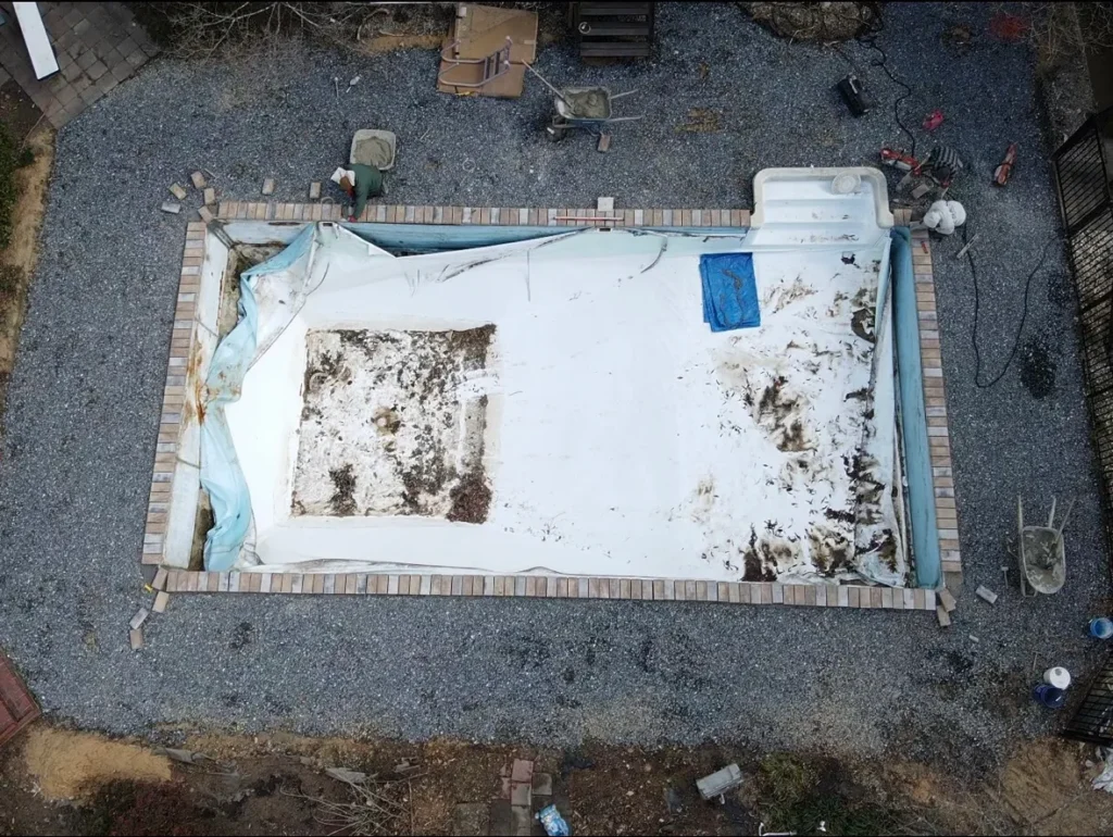 Empty rectangular pool under renovation with torn liner and debris inside