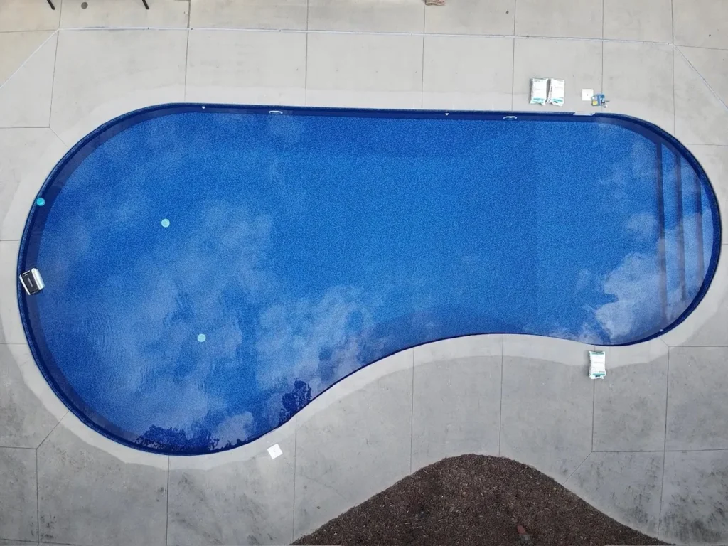 Kidney-shaped pool with new blue liner and filled with clear water, aerial view