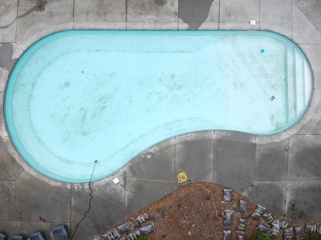 Kidney-shaped pool drained and prepared for renovation, viewed from above
