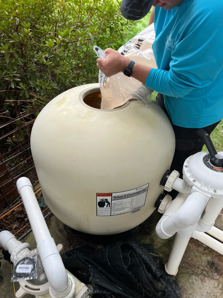 Technician pouring sand into a Triton II pool filter during maintenance
