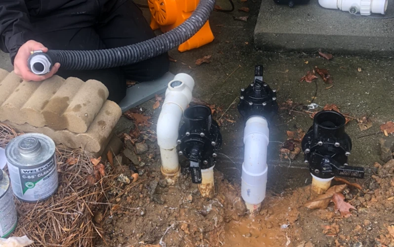 A man cleans a pipe using a hose, directing water to remove dirt and debris effectively.