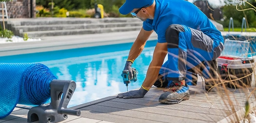A man in a red shirt and hat is working on a pool, focused on maintenance tasks under bright sunlight.